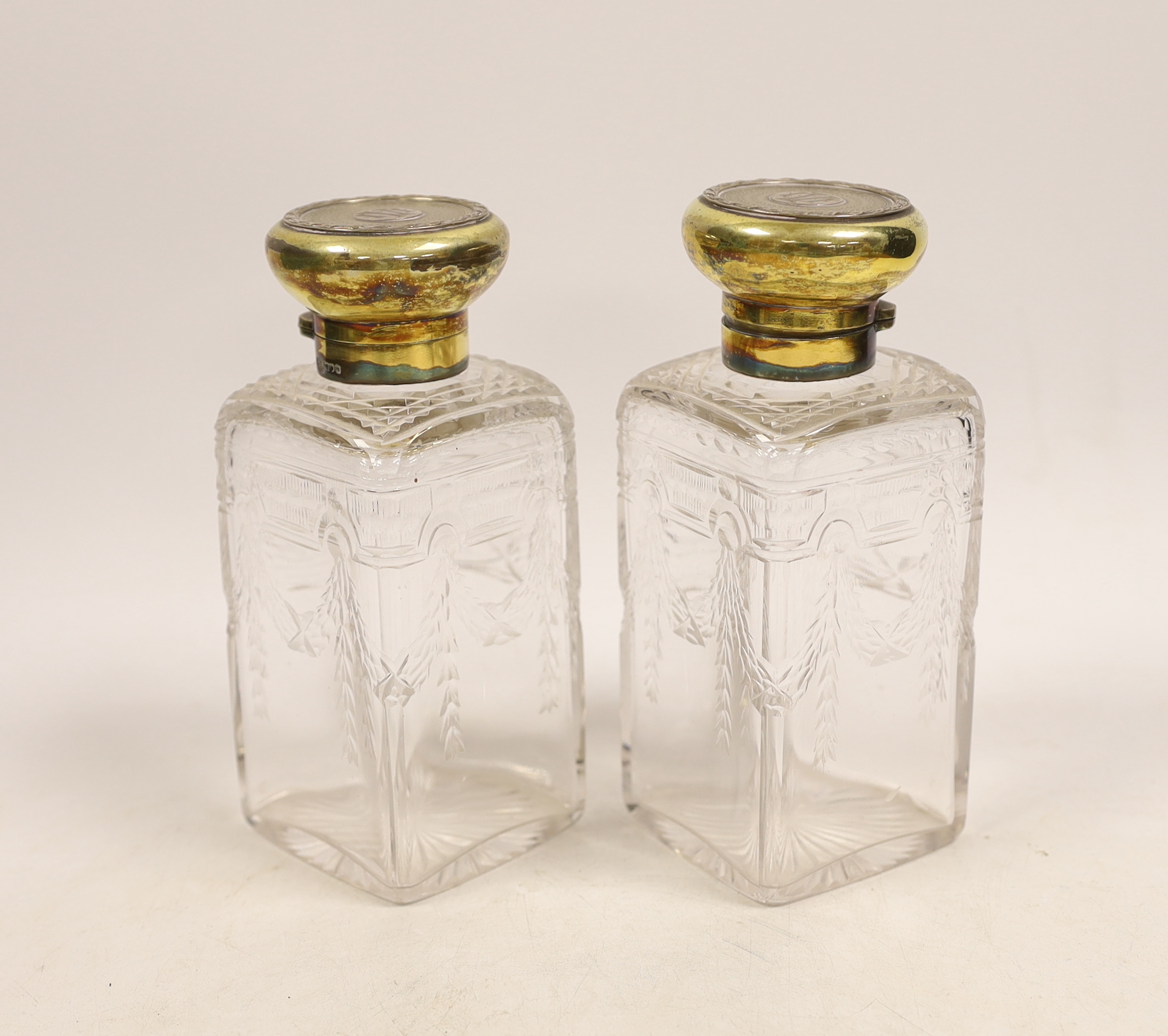 A pair of George V silver gilt mounted cut and etched glass square scent bottles and stoppers, Goldsmiths & Silversmiths Co Ltd, London, 1911, 15cm.